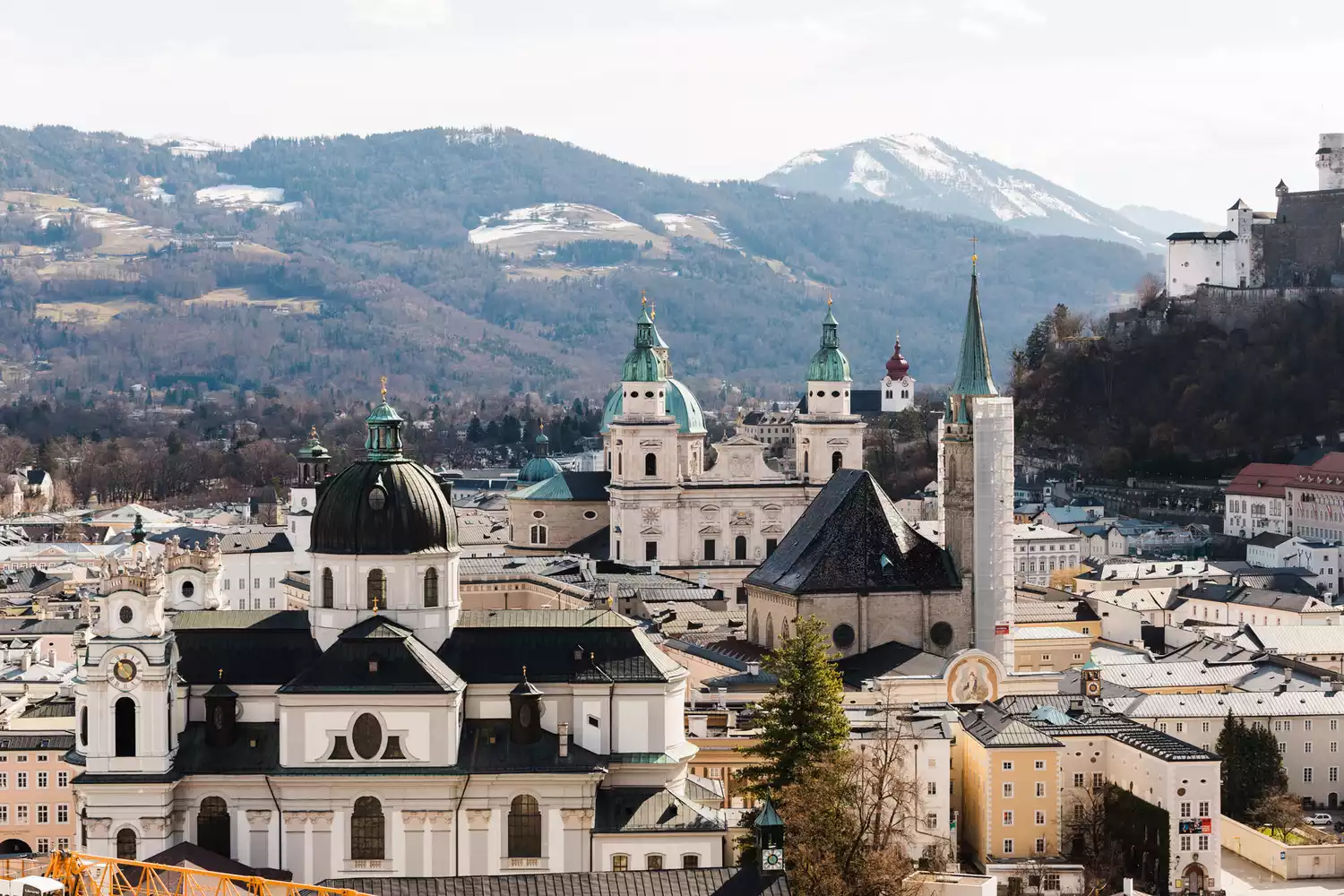 The city skyline of Salzburg featuring historic domes and spires against a distant mountain backdrop.