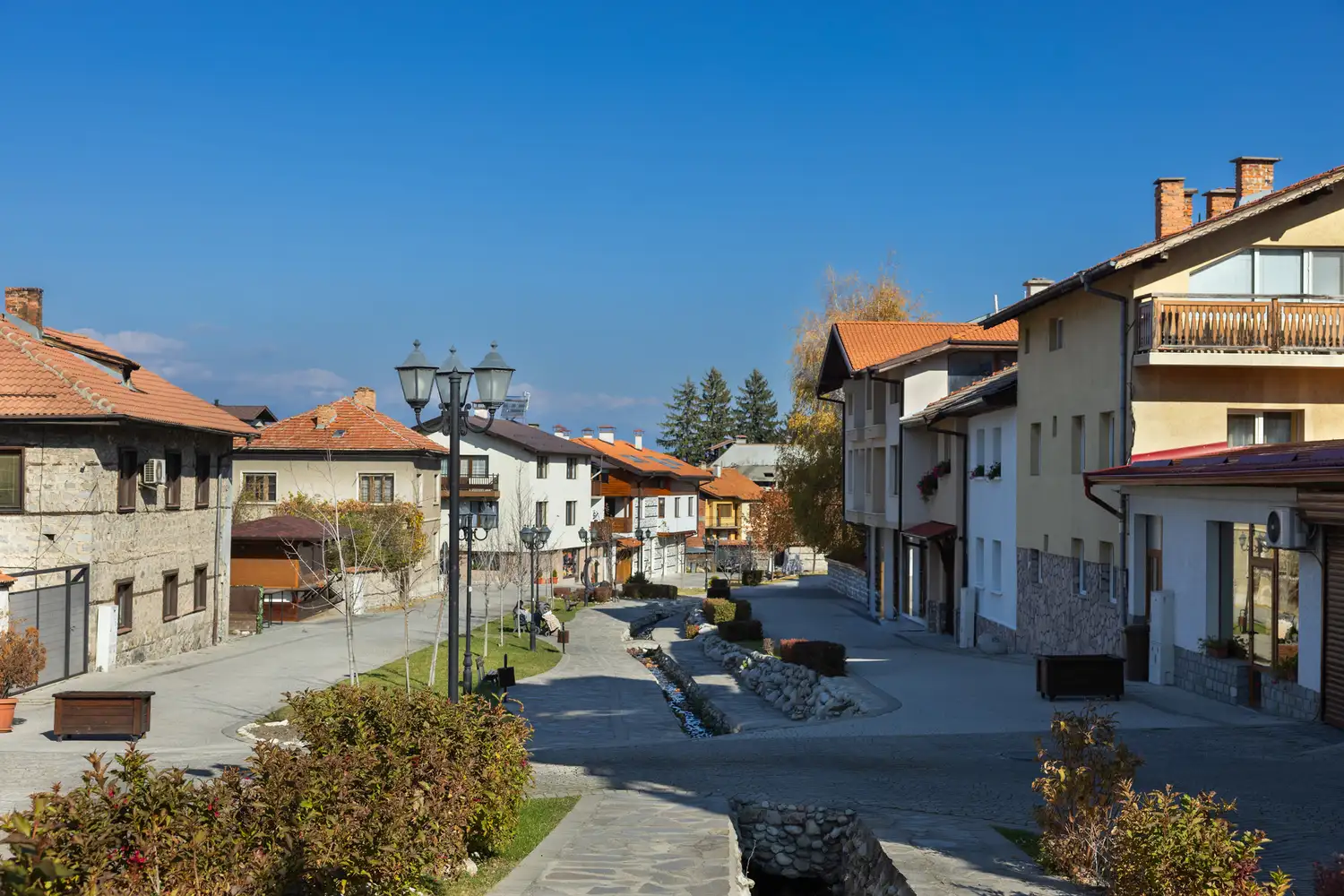 A stone pathway in Bansko flanked by traditional Bulgarian houses with a mountain in the distance.