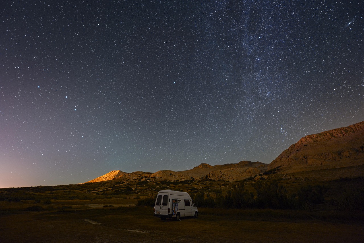 Cozy interior of a camper van with a made-up bed and a view out the back doors.