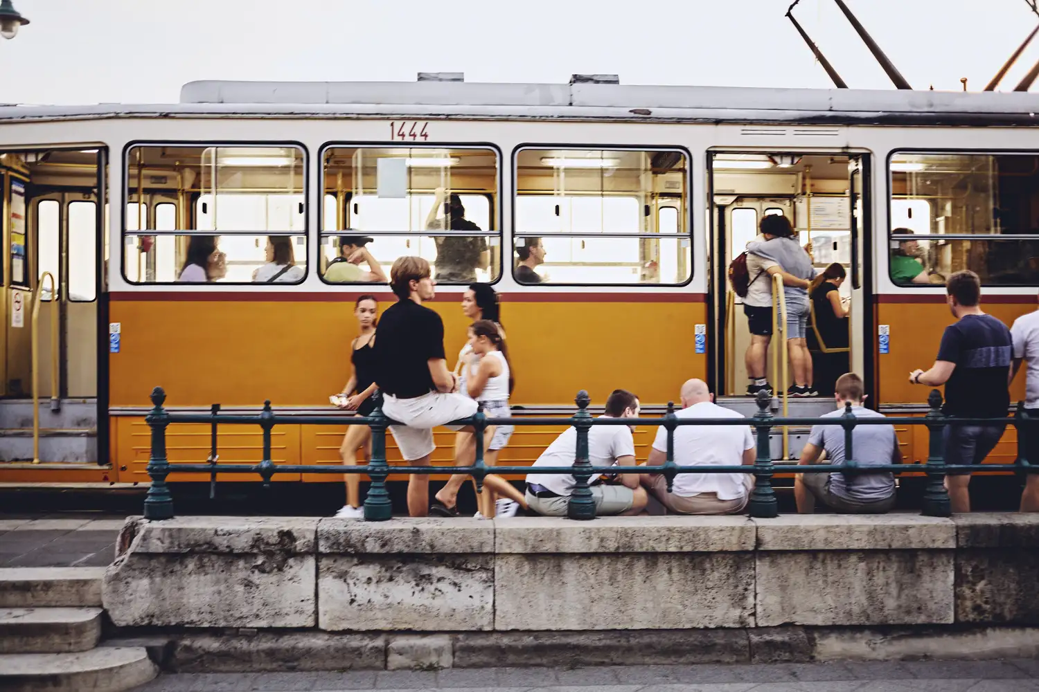 A classic bright yellow tram on a street in Budapest with passengers nearby.
