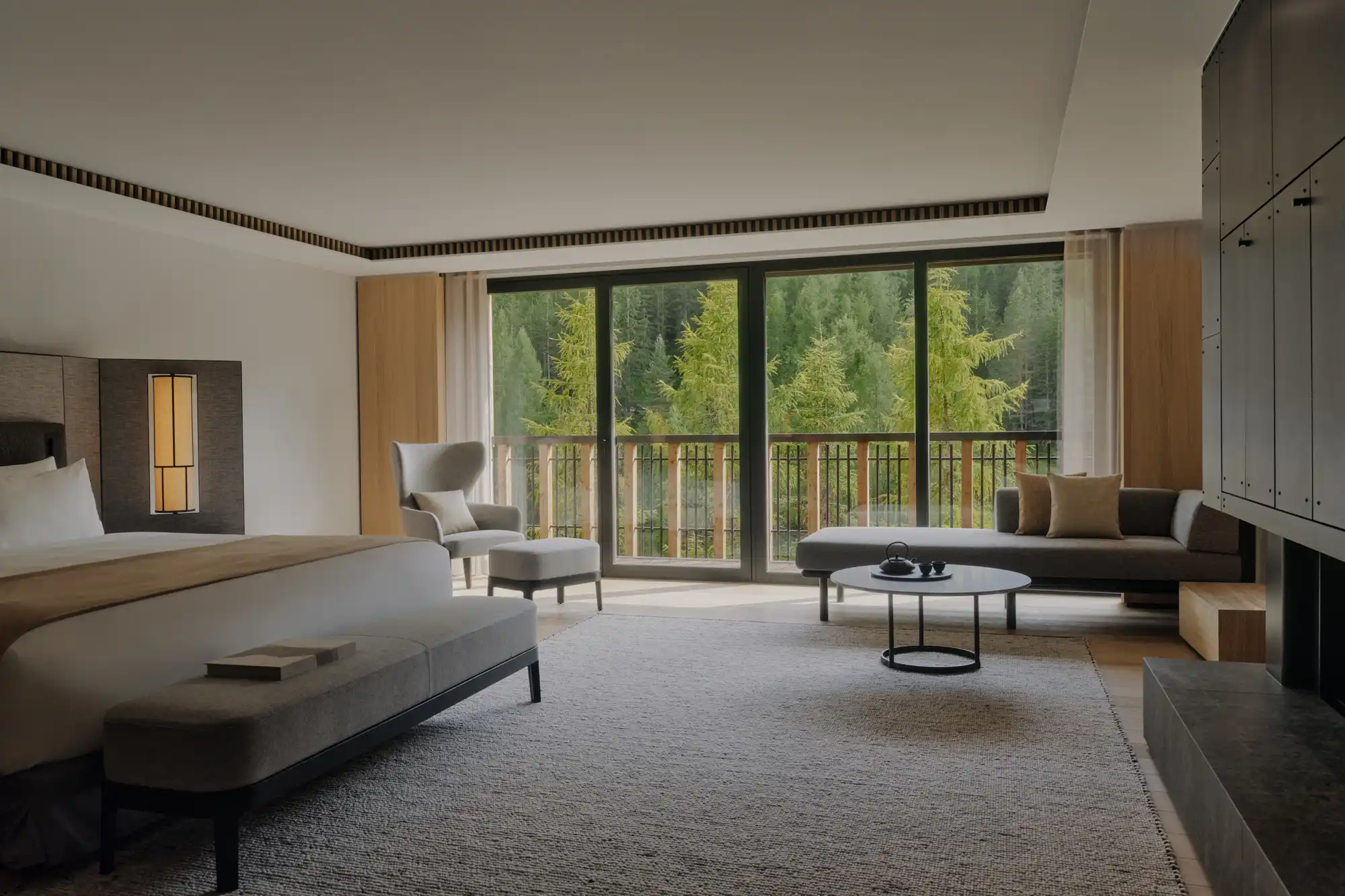 A modern Aman suite bedroom with large windows framing a lush green forest view.