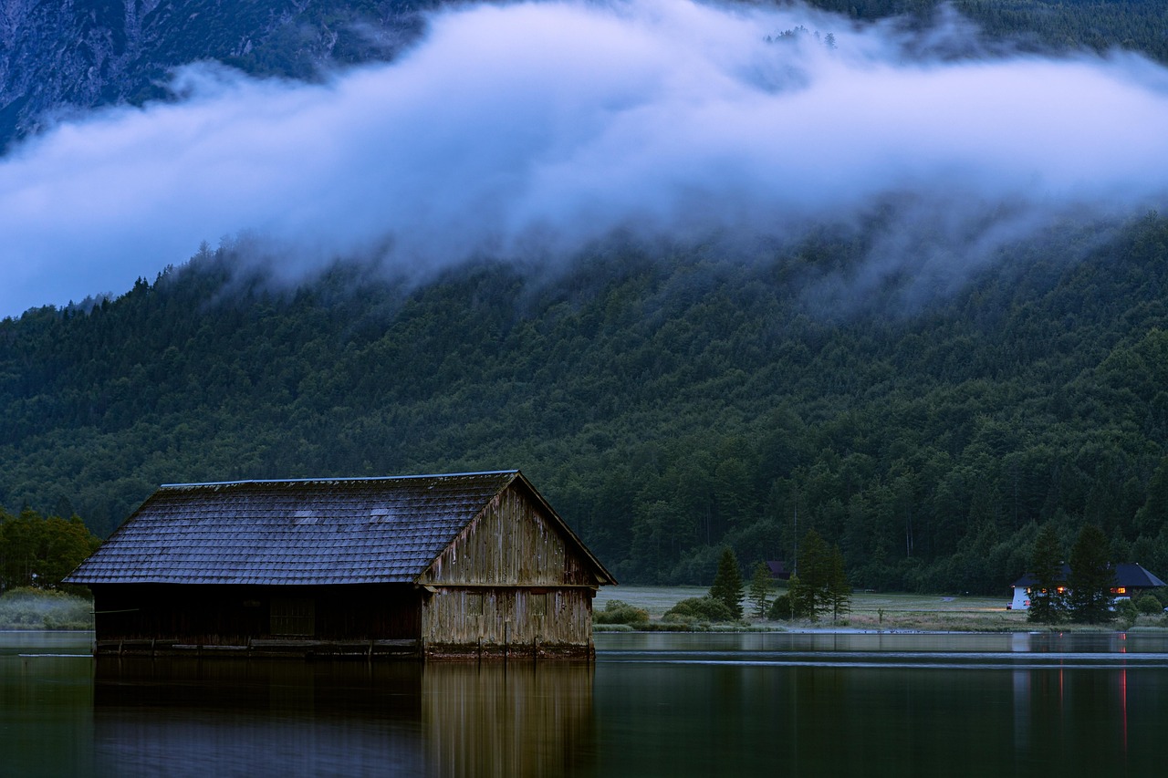 A small wooden cabin on the edge of a calm lake surrounded by colorful autumn trees.