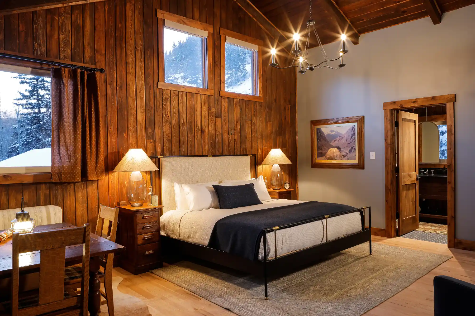 A master bedroom in a luxury mountain cabin with a large wooden bed, rustic timber walls, and a window overlooking a snow-covered forest.