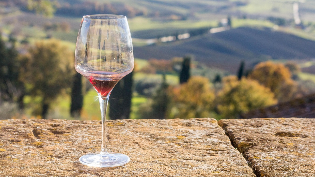 A wine glass on a wooden table overlooking a vast vineyard and mountain cliffs