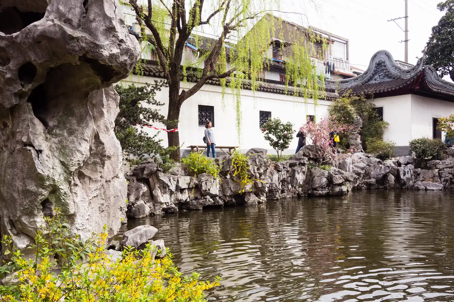 A serene garden with a pond traditional architecture and people walking along a rocky pathway.