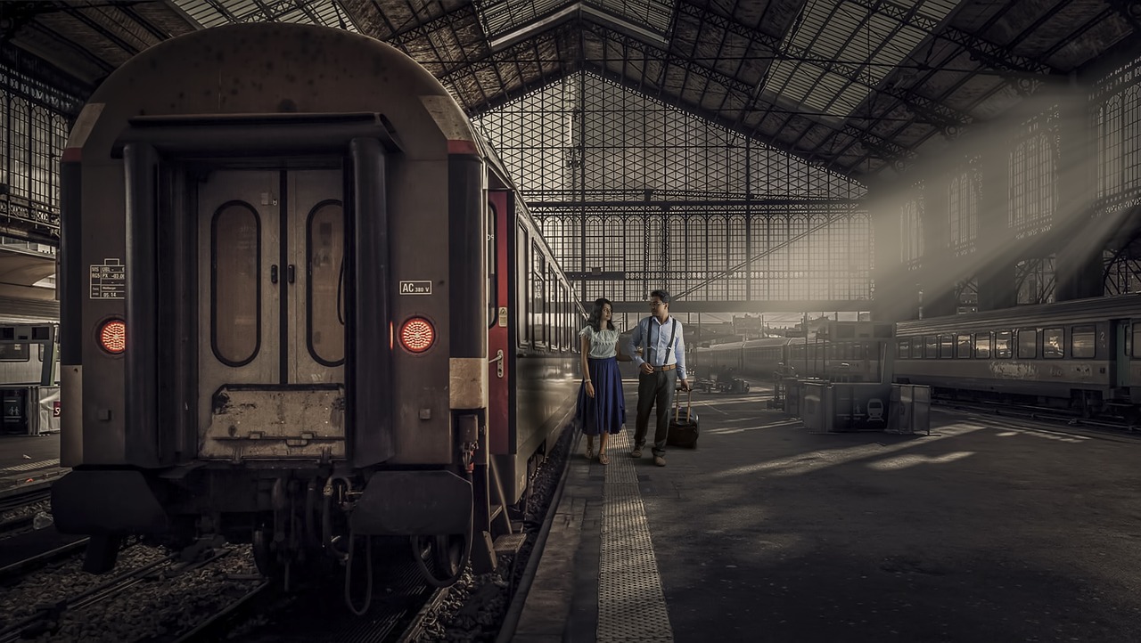 A traveler with a single sleek backpack walking along a train platform toward a departing train.