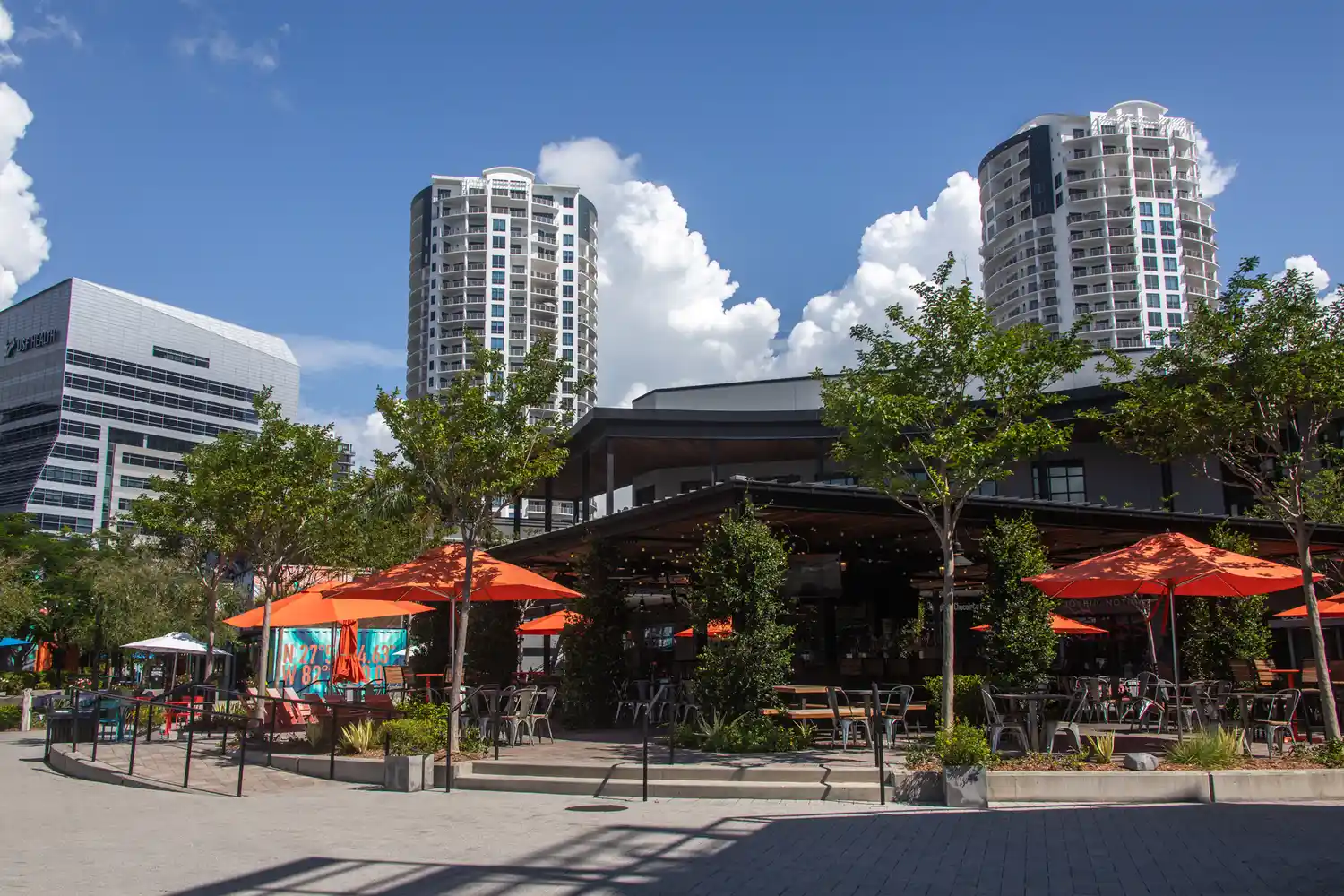 Outdoor seating and umbrellas at Sparkman Wharf in Tampa, Florida, surrounded by modern buildings.