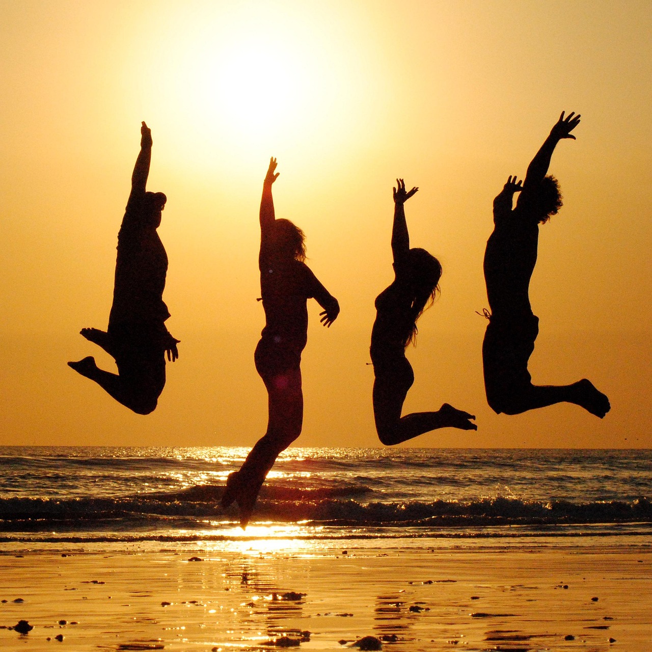 Silhouettes of two people sitting on a beach watching a dramatic orange sunset.