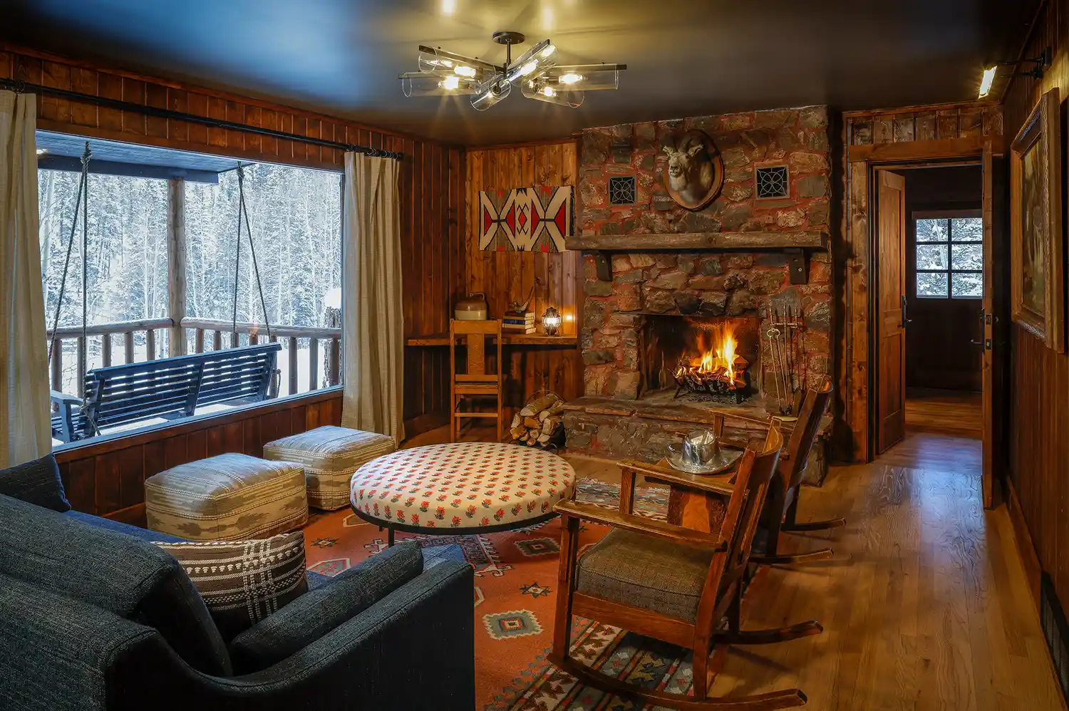 A luxury rustic living room with a stone fireplace, wooden walls, and comfortable rocking chairs.