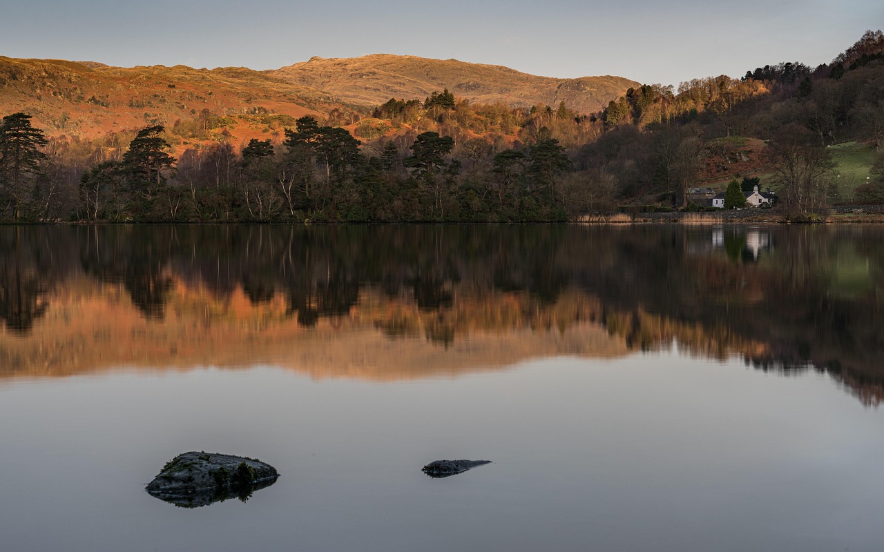 A calm lake reflecting green mountains under a soft English sky.