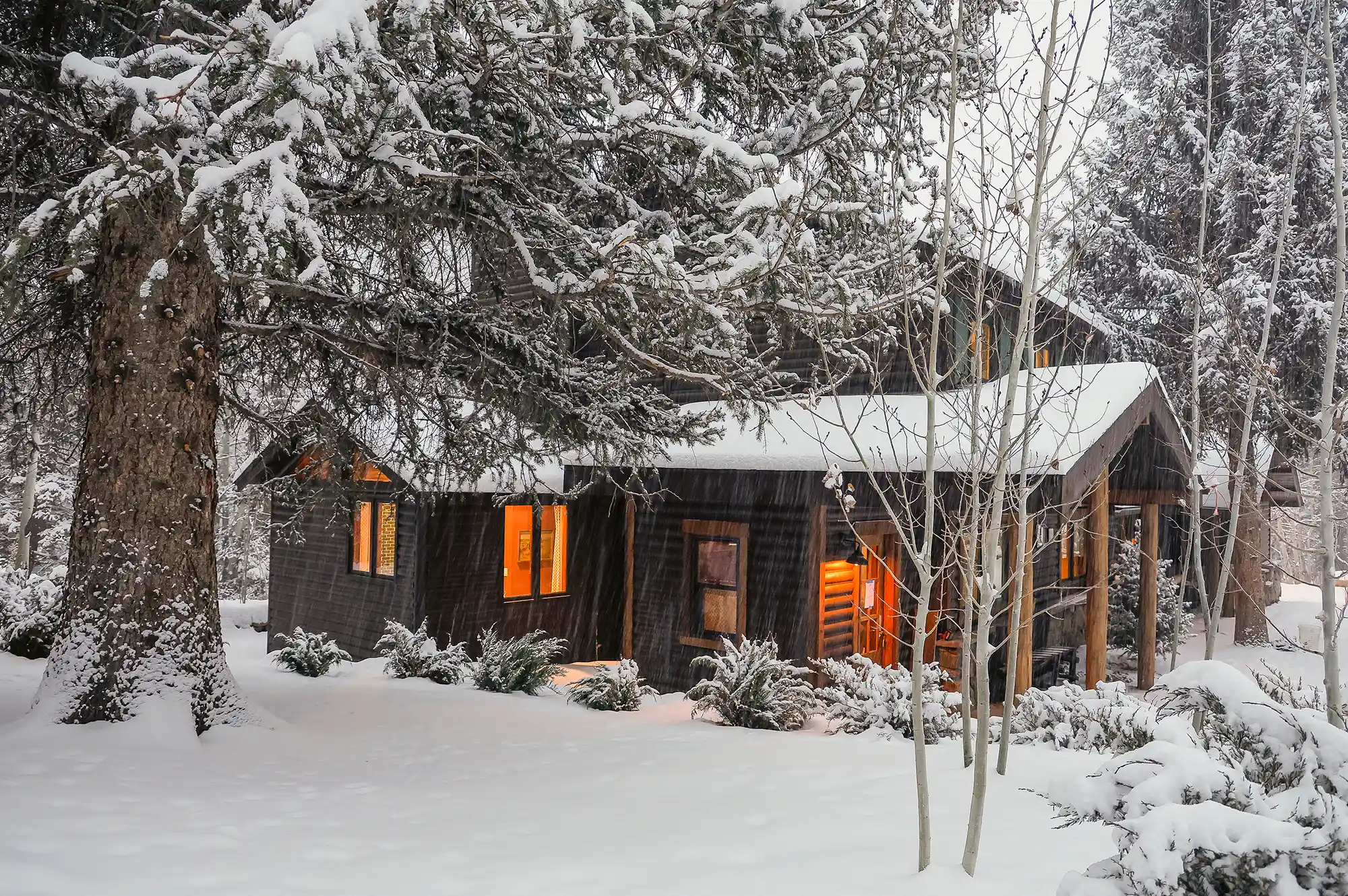 A snow-covered log cabin glowing with warm light at night in the forest.