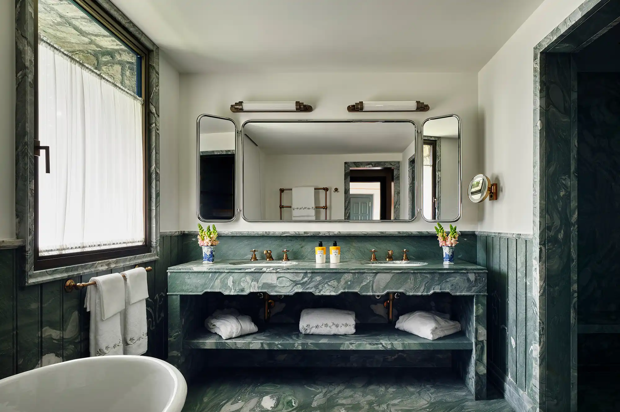 A luxury hotel bathroom featuring twin sinks with premium marble countertops and gold-toned fixtures.