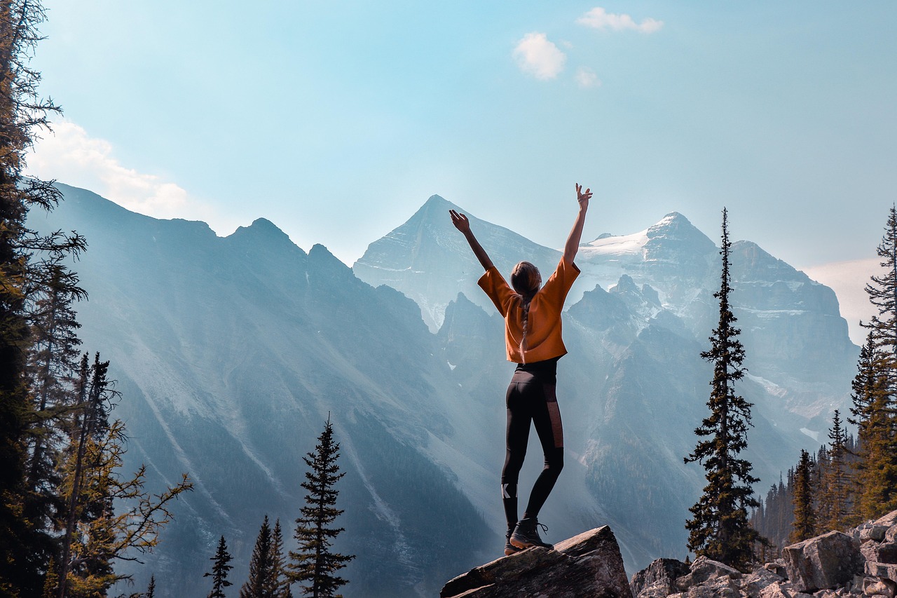 A woman standing alone on a snowy mountain peak, looking out over a vast wilderness.