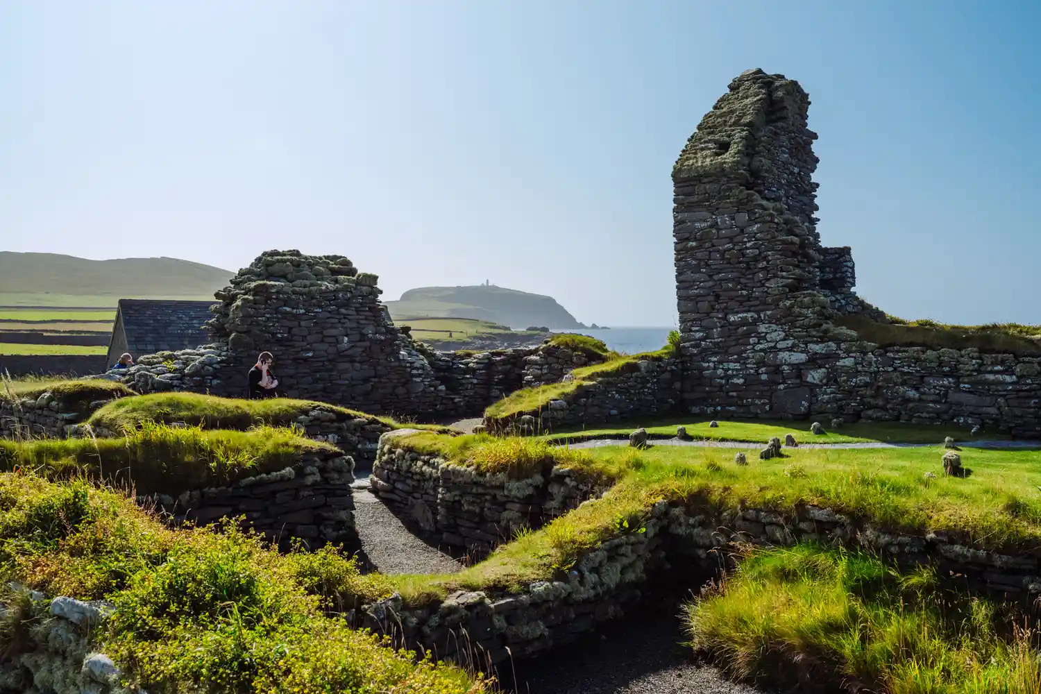 The stone ruins of the Jarlshof prehistoric settlement surrounded by green grass.
