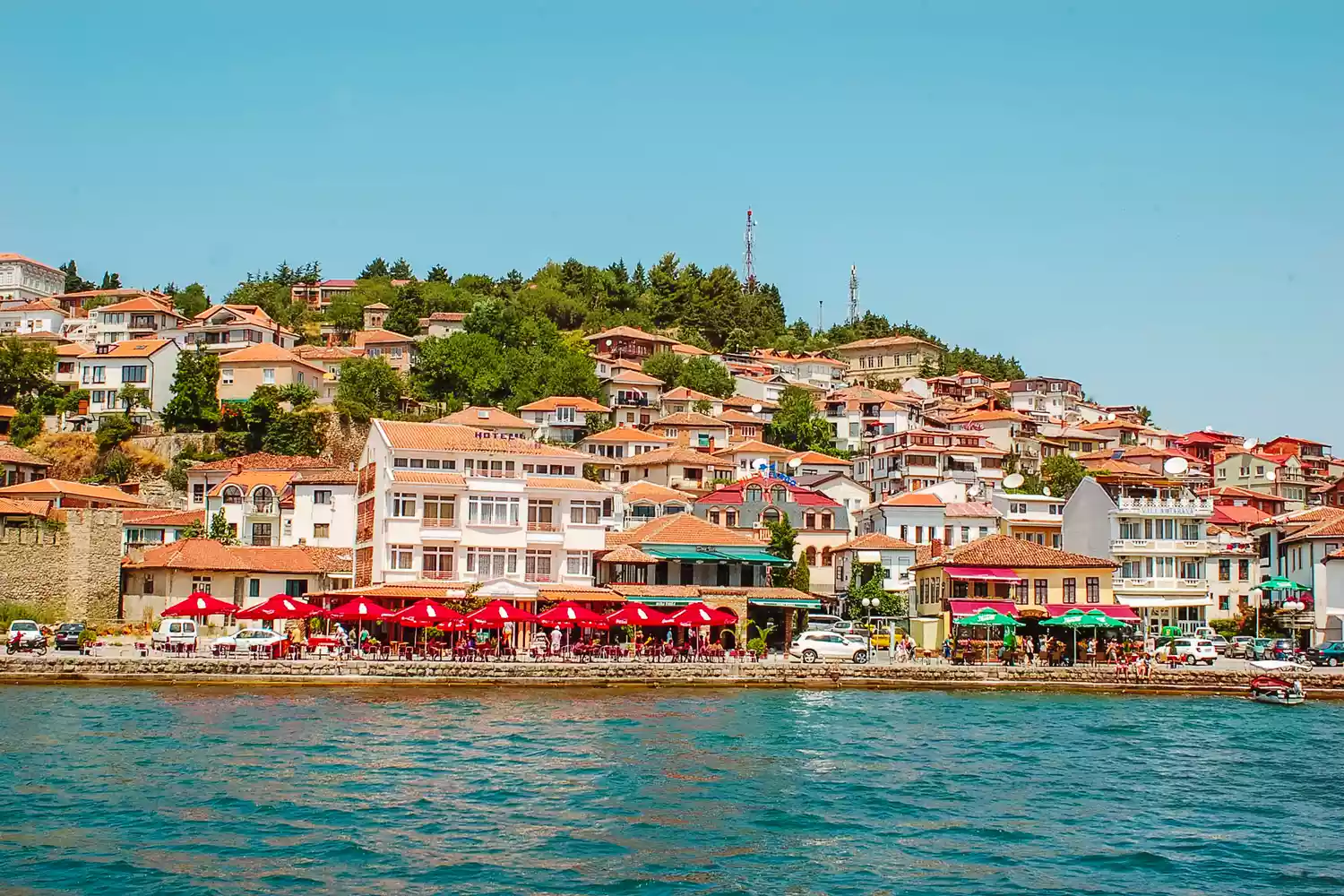 A picturesque view of a traditional town on the shores of Lake Ohrid with hills in the background.
