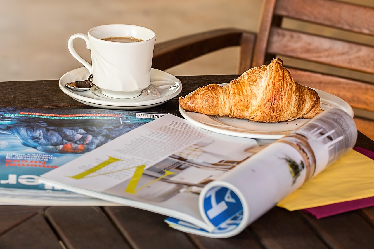 A close-up of a cup of coffee and medialunas on a sunlit table.