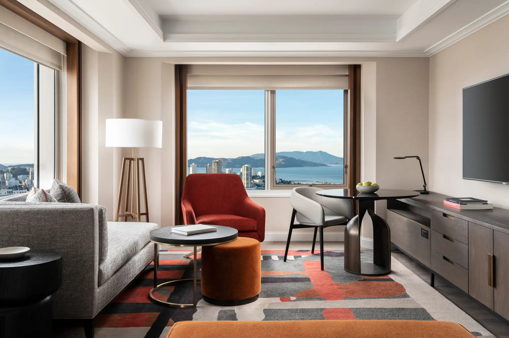 Spacious luxury hotel living room with panoramic city and waterfront views through floor-to-ceiling windows.