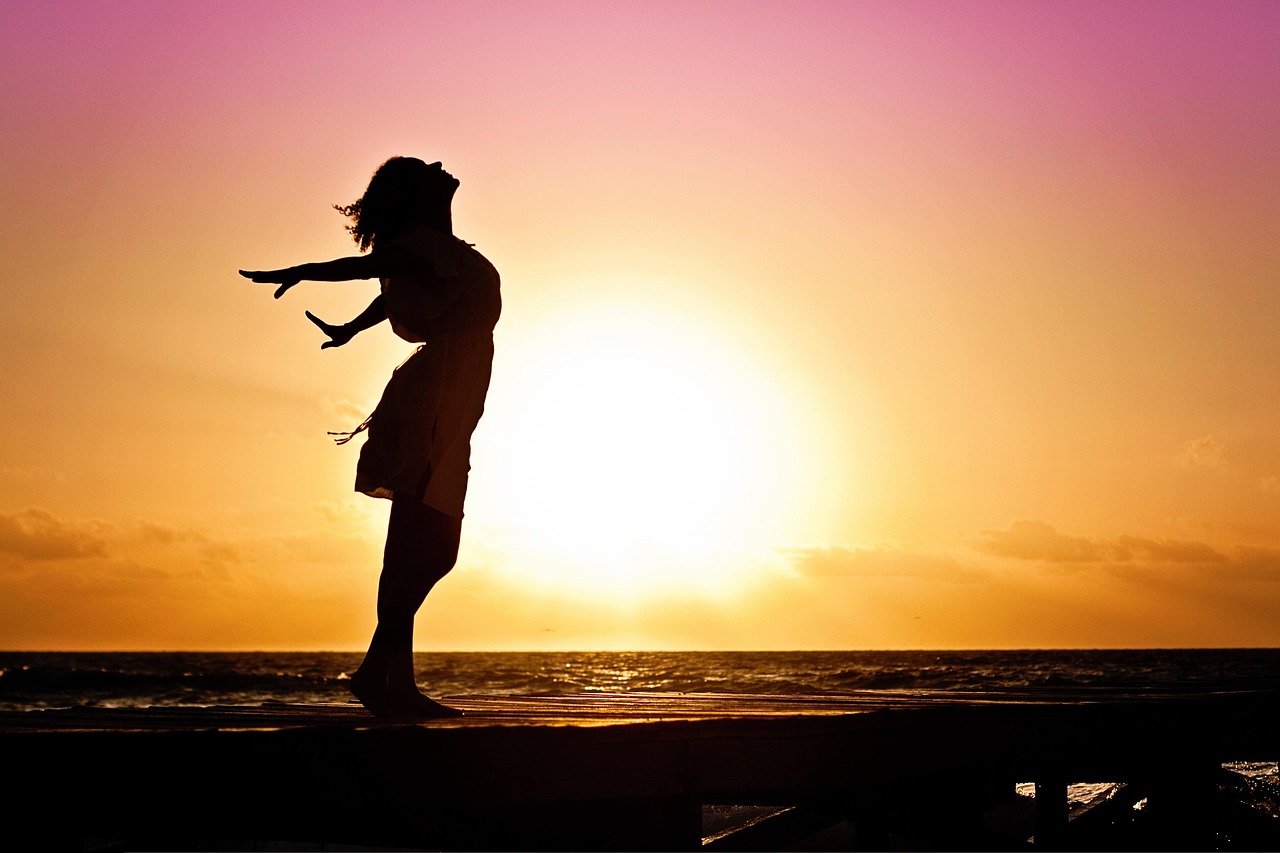 A woman sitting alone by the ocean during a golden sunset