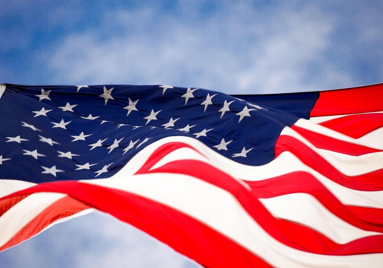An American flag waving with bright fireworks in the background night sky.