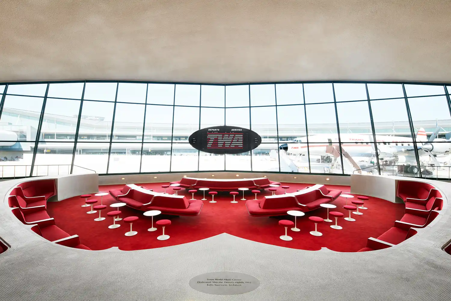 The interior of the TWA Hotel terminal with view of the tarmac through large windows.