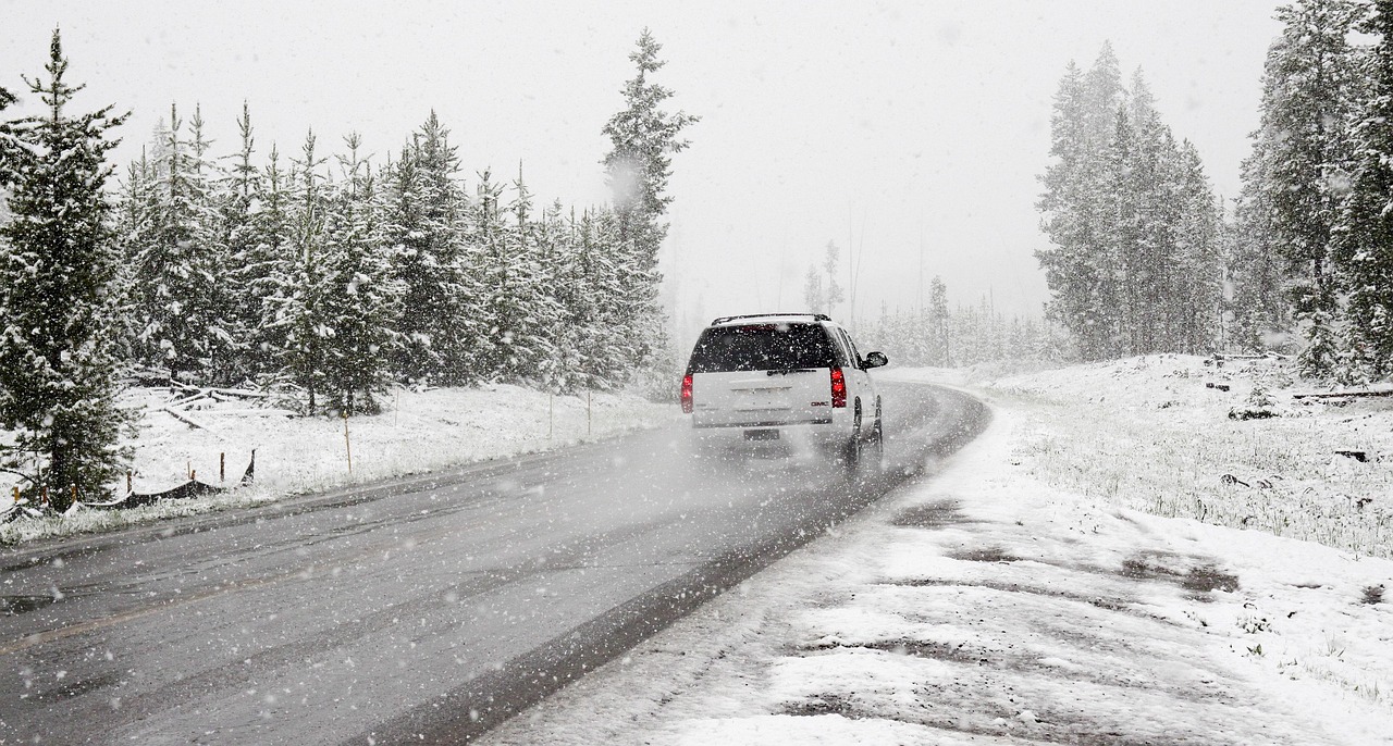 A vehicle driving through a narrow, snow-covered road lined with tall trees.
