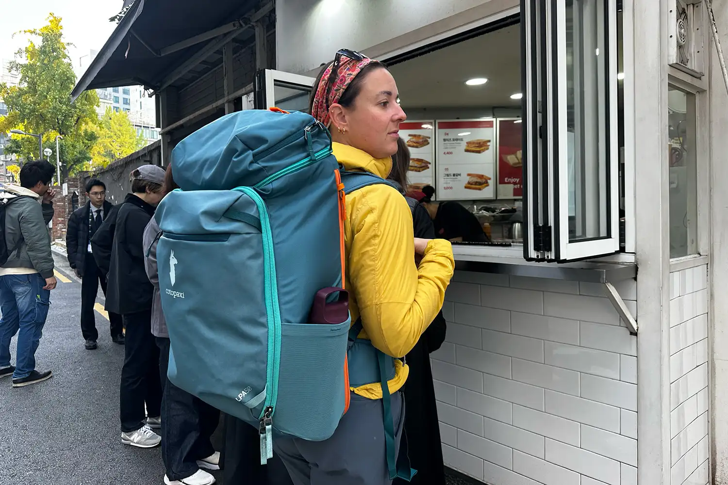 A traveler with a large backpack standing at a street food counter in Southeast Asia.