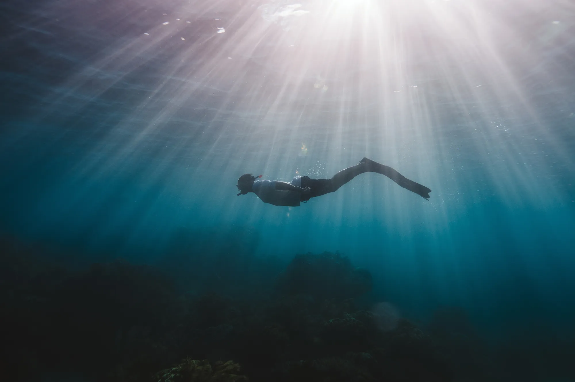A person snorkeling under the surface of the ocean with sunbeams piercing through the water.