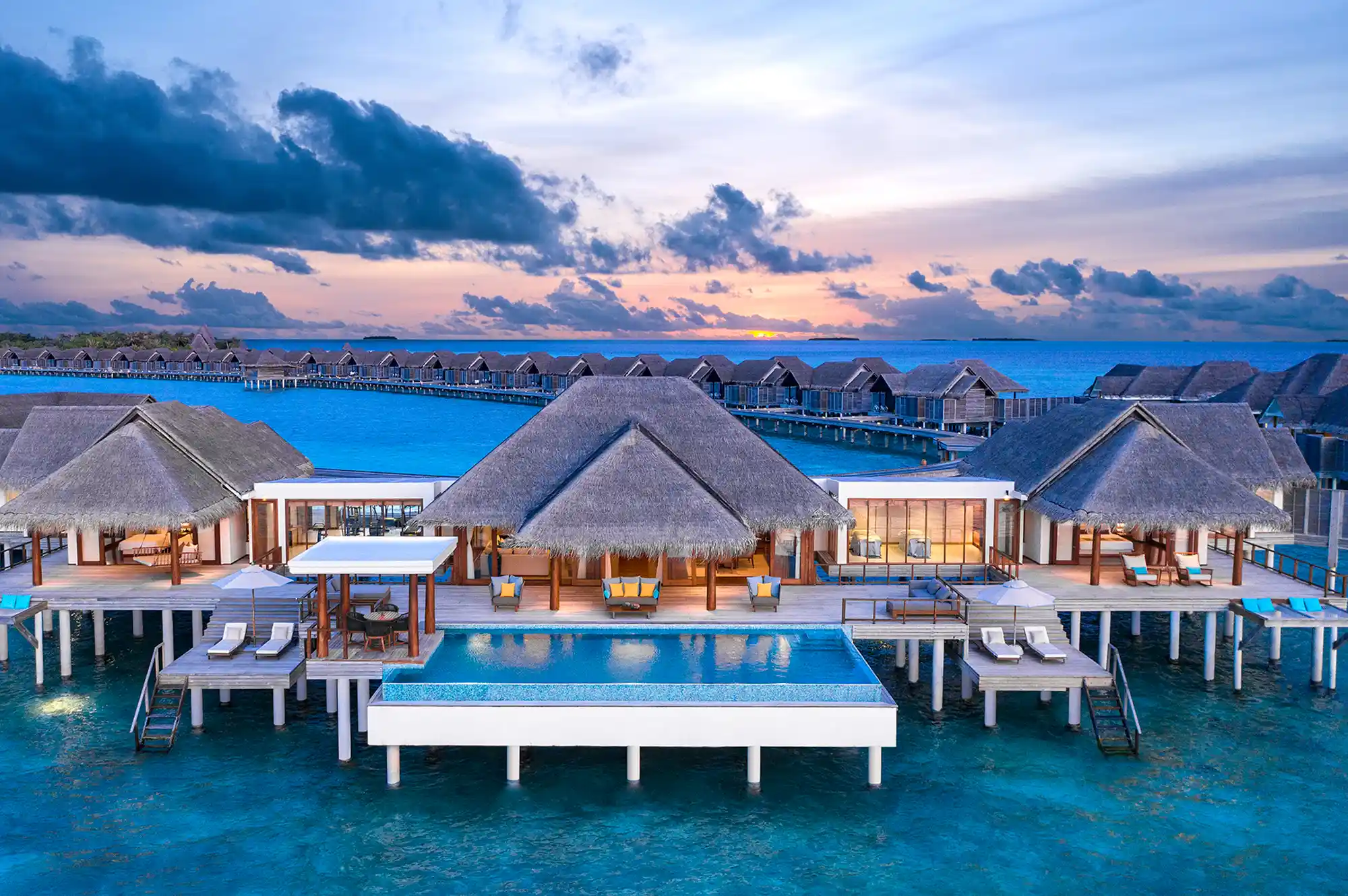 Aerial view of thatched-roof overwater villas extending into the turquoise ocean.