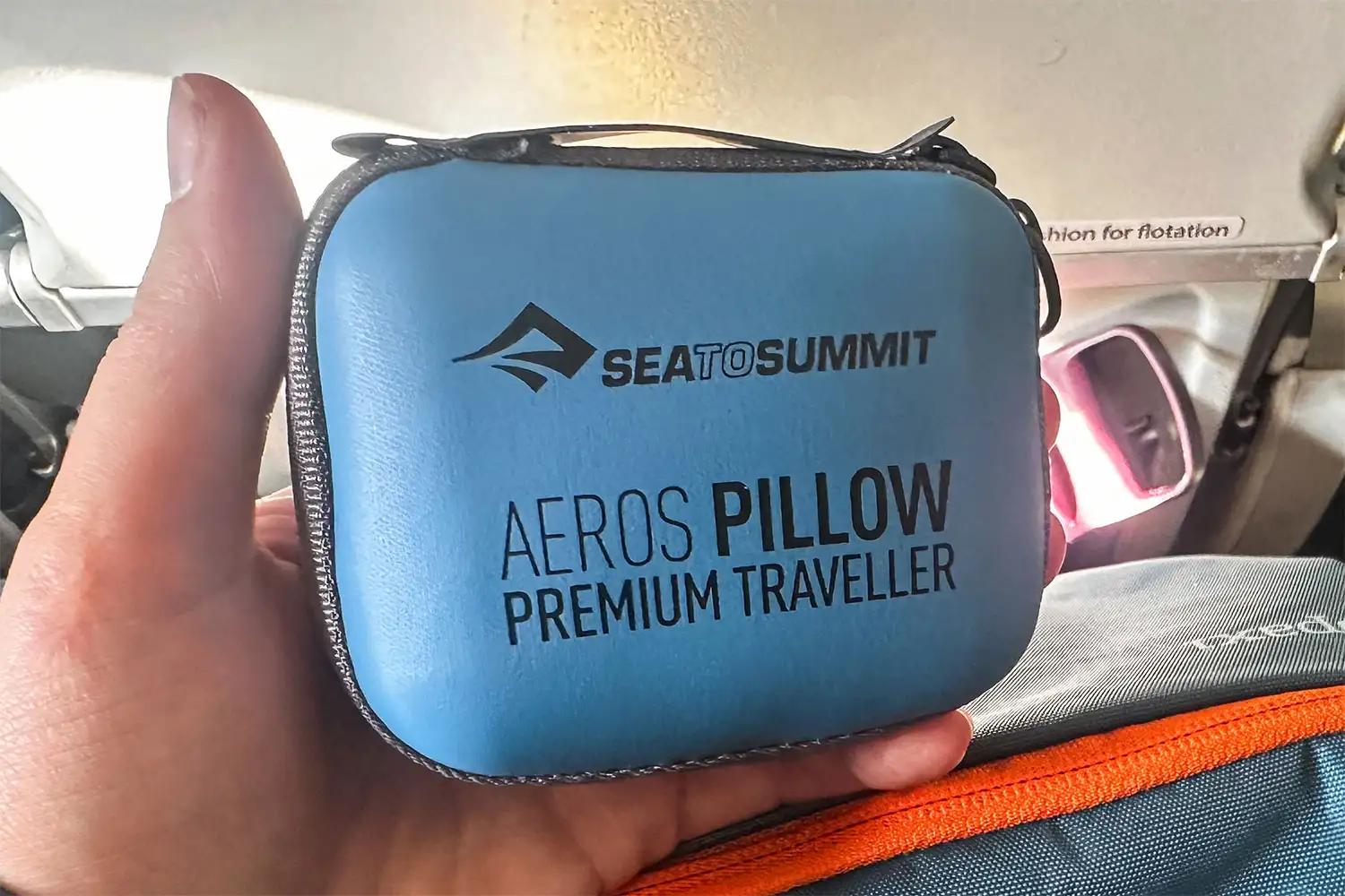 A hand holding a compact Sea to Summit travel pillow in an airplane cabin environment.
