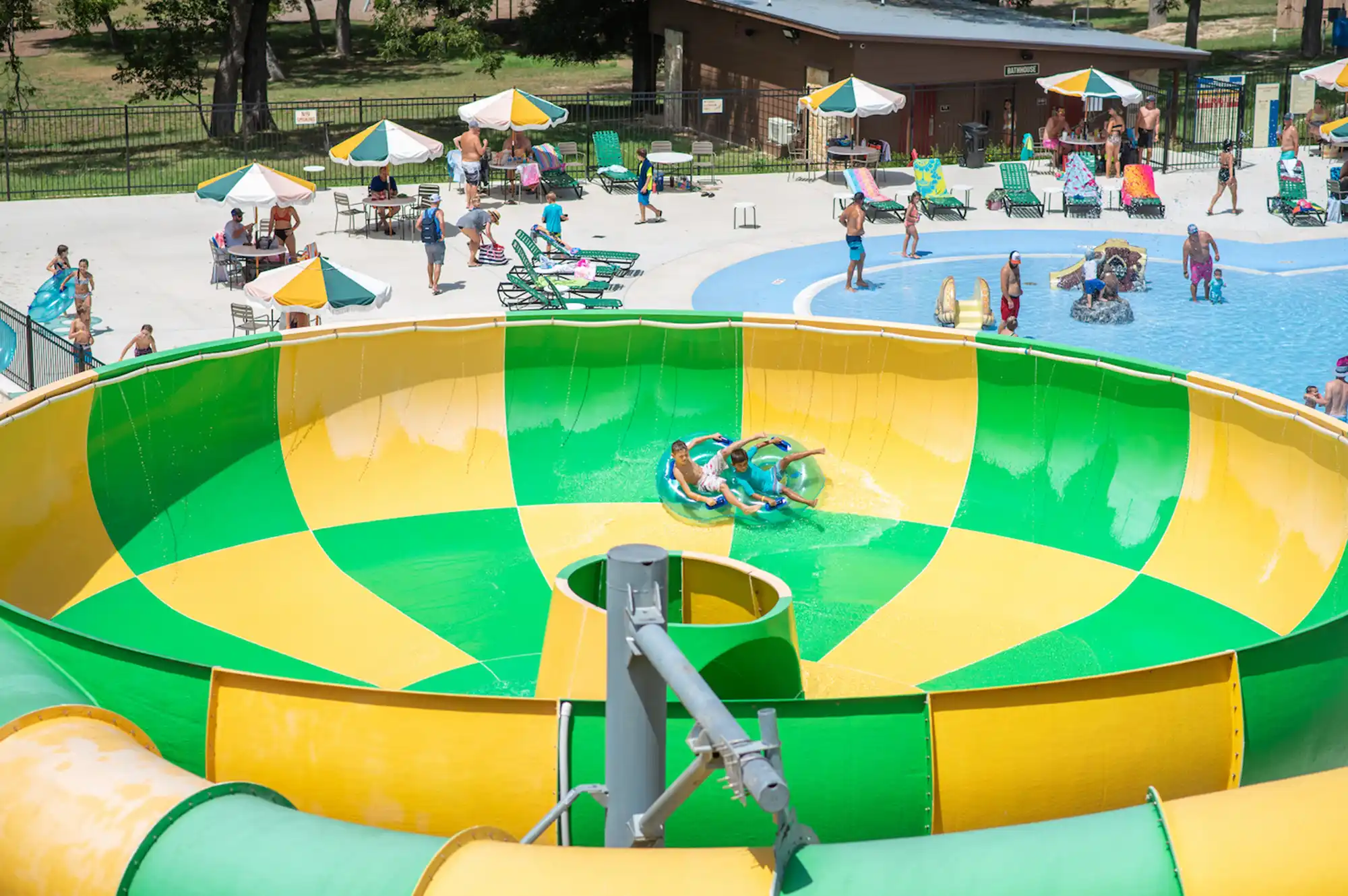 Families riding a large blue and white funnel-shaped water slide at a resort park.