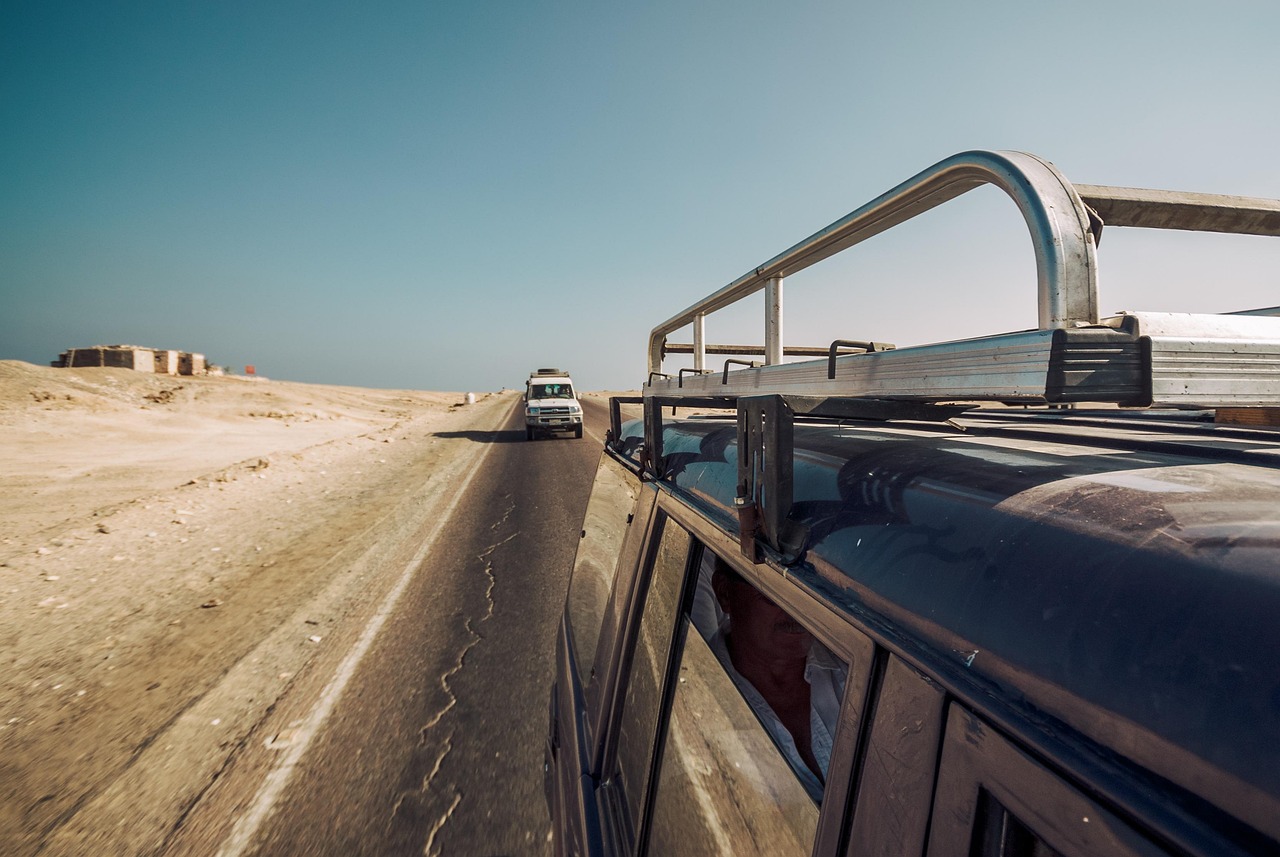 A single vehicle parked in a vast, beautiful desert landscape under a clear blue sky.