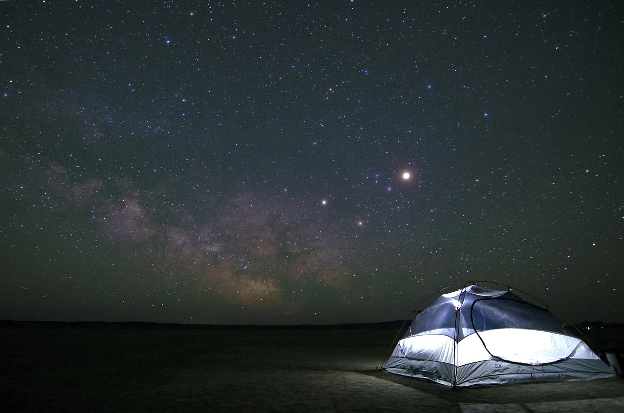 A luxury safari tent glowing from within under a starry night sky in the desert.