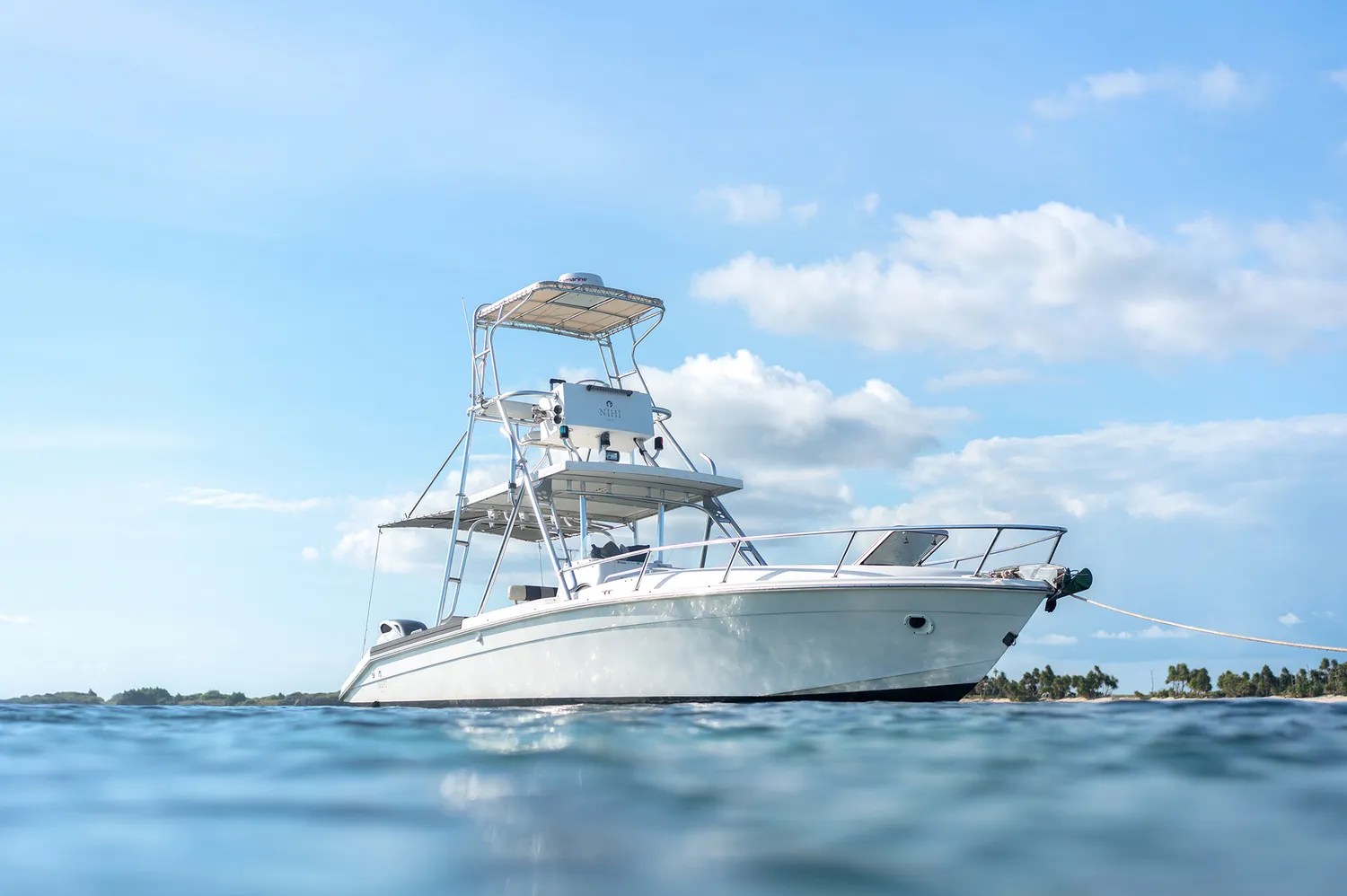 A white motorboat anchored in crystal clear shallow water near a remote beach.
