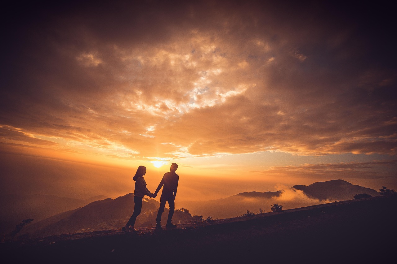 A group of skiers silhouetted against a golden sunset on a high mountain ridge.